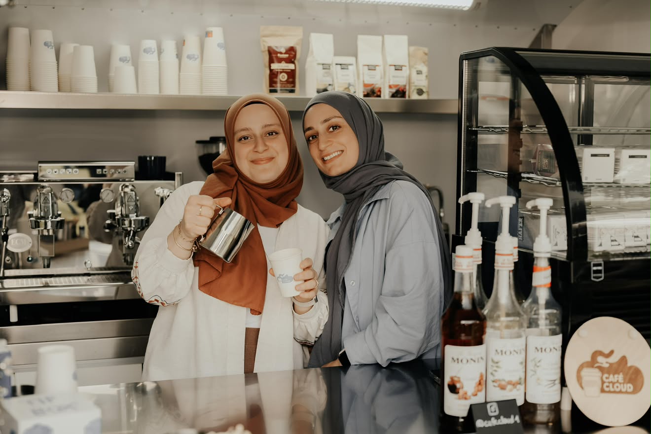 Sümeyra gießt Milch auf, Melek hält einen Café Cloud Becher